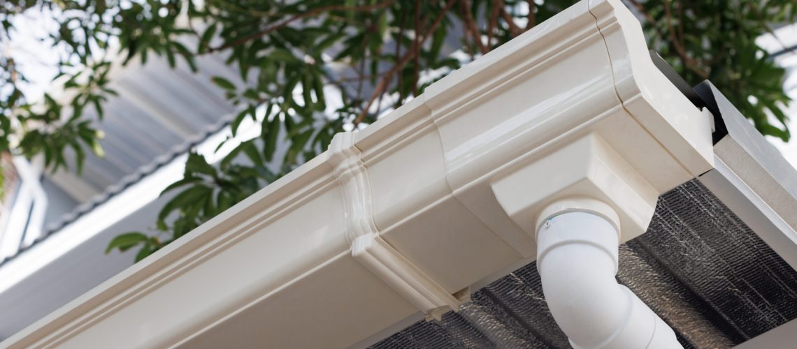 white plastic rain gutter of roof of house. vinyl rain gutter and downpipe.
